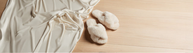 Stivaletti invernali EMU Australia in suede grigio con fodera in pelliccia, appoggiati su sfondo verde petrolio accanto a un morbido tessuto in lana.