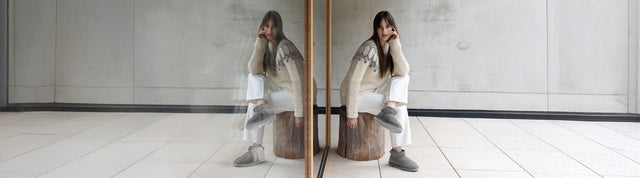 Stivaletti invernali EMU Australia in suede grigio con fodera in pelliccia, appoggiati su sfondo verde petrolio accanto a un morbido tessuto in lana.