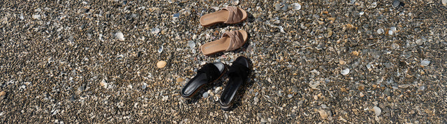 Stivaletti invernali EMU Australia in suede grigio con fodera in pelliccia, appoggiati su sfondo verde petrolio accanto a un morbido tessuto in lana.