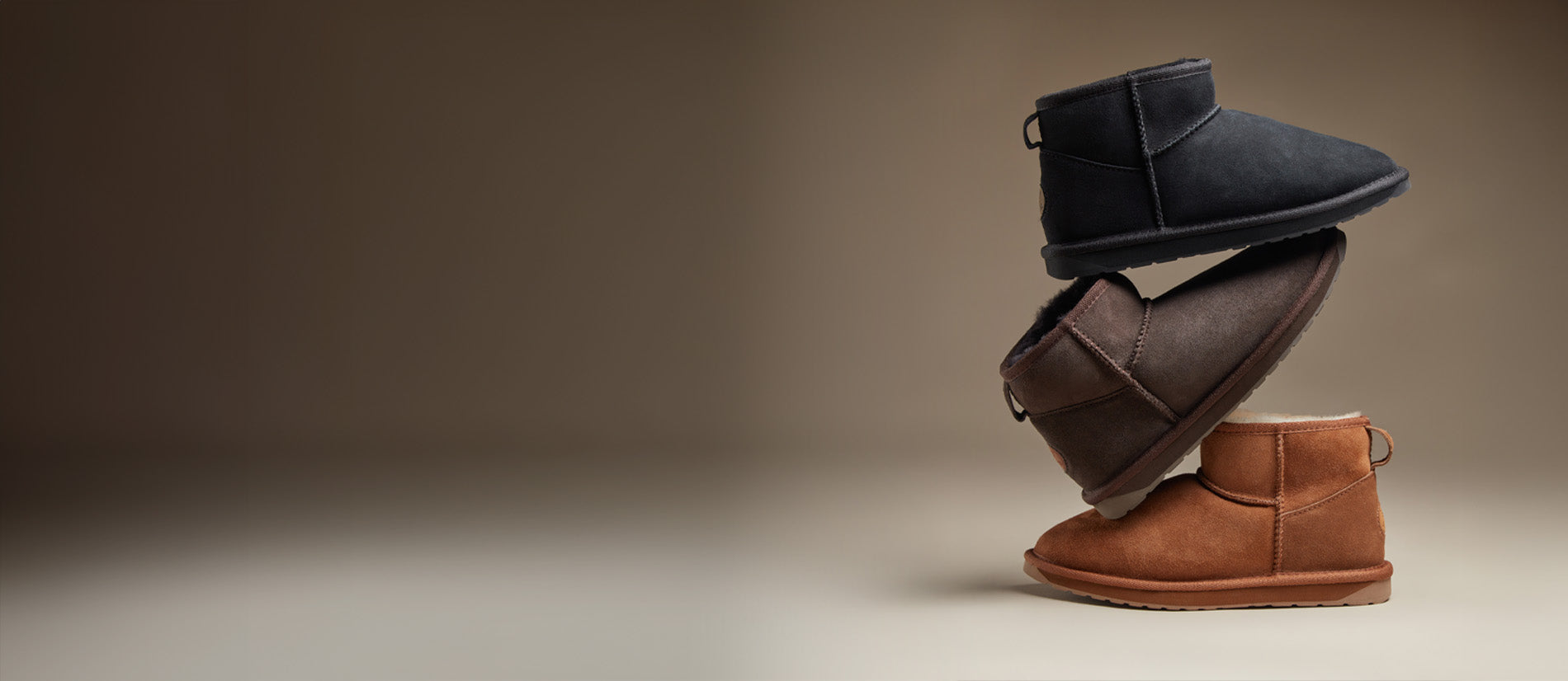 Tre paia di stivaletti in suede da donna in diversi colori — nero, marrone e cuoio — impilati su sfondo neutro, collezione invernale lifestyle disponibile su Amuvia.