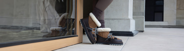Stivaletti impermeabili EMU Australia da donna in pelle marrone con interno shearling e suola carrarmato, indossati all’aperto.
