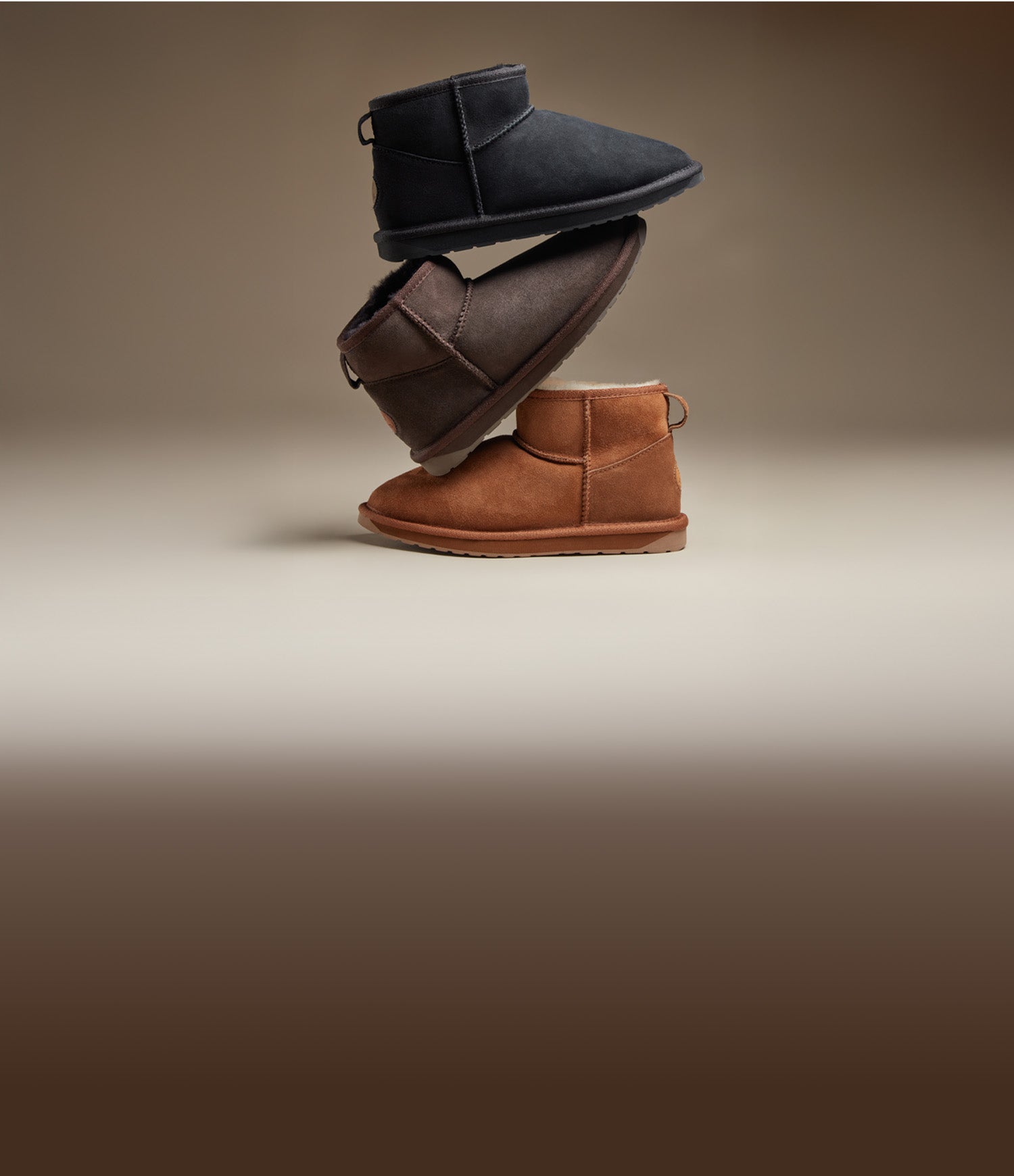 Tre paia di stivaletti in suede da donna in diversi colori — nero, marrone e cuoio — impilati su sfondo neutro, collezione invernale lifestyle disponibile su Amuvia.