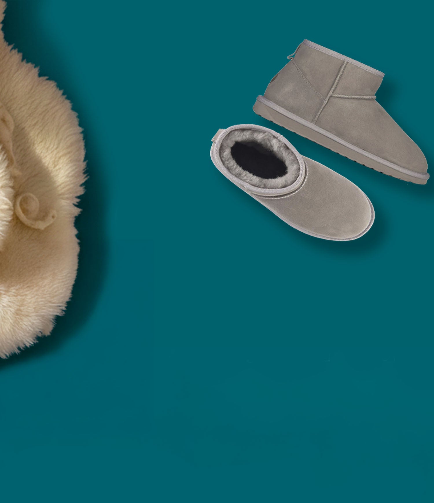 Stivaletti invernali EMU Australia in suede grigio con fodera in pelliccia, appoggiati su sfondo verde petrolio accanto a un morbido tessuto in lana.