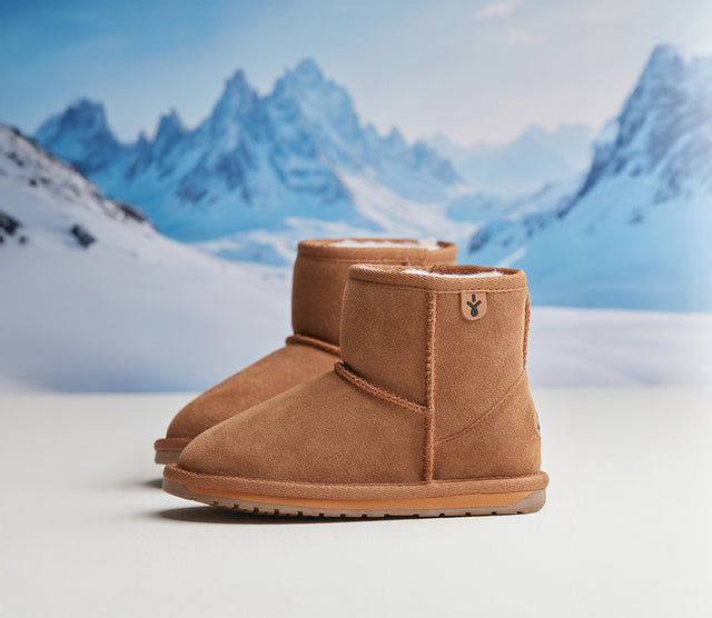 Stivaletti EMU Australia Stinger Mini da donna in pelle scamosciata color cuoio con fodera in lana merino, ideali per l’inverno e il tempo libero, fotografati davanti a paesaggio montano innevato.