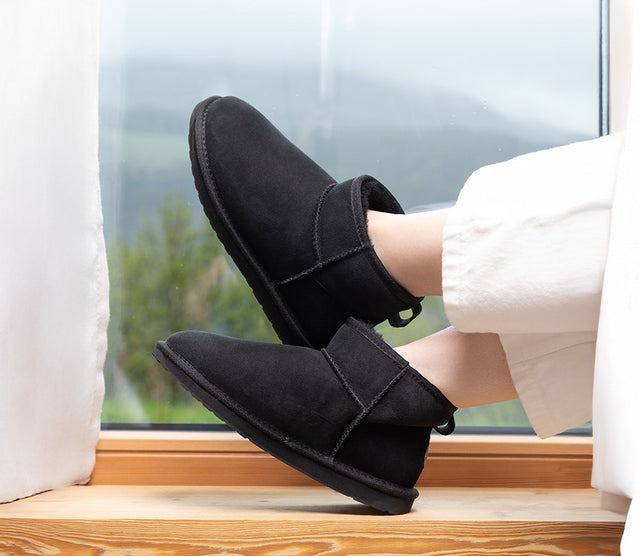 Stivaletti neri EMU Australia da donna in pelle scamosciata con fodera in lana merino, indossati in casa davanti alla finestra.