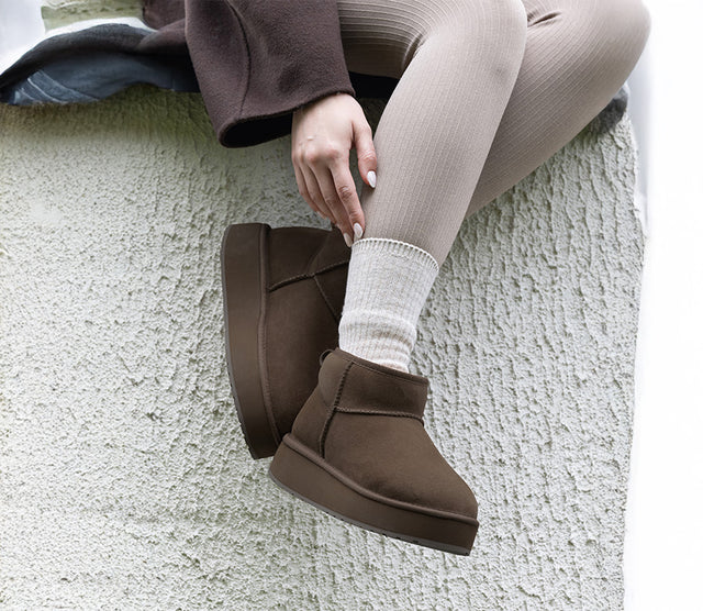 Stivaletti neri EMU Australia da donna in pelle scamosciata con fodera in lana merino, indossati in casa davanti alla finestra.