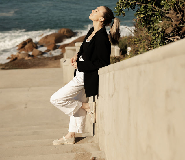 Sandali donna EMU Australia in pelle intrecciata tenuti in mano su spiaggia sabbiosa