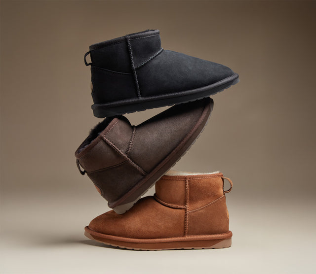 Tre stivaletti EMU Australia Stinger Mini da donna in pelle scamosciata, nei colori nero, marrone e cognac, impilati in composizione studio.