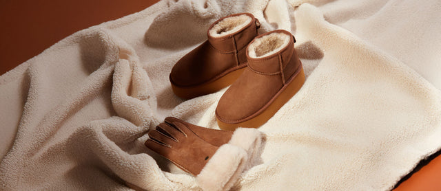 Stivaletti platform e guanti EMU Australia in pelle scamosciata color cuoio con fodera in lana merino, poggiati su una coperta in shearling color panna, rappresentazione di comfort e calore invernale.