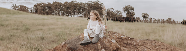 bambina in mezzo alla natura seduta su un sassa che indossa stivaletto con il pelo wallaby shaun the sheep grigio