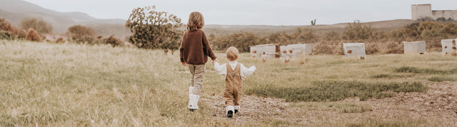 bambini mano nella mano girati di schiena che camminano in campagna e indossano stivaletti bianchi e neri con pelo emu australia shaun the sheep